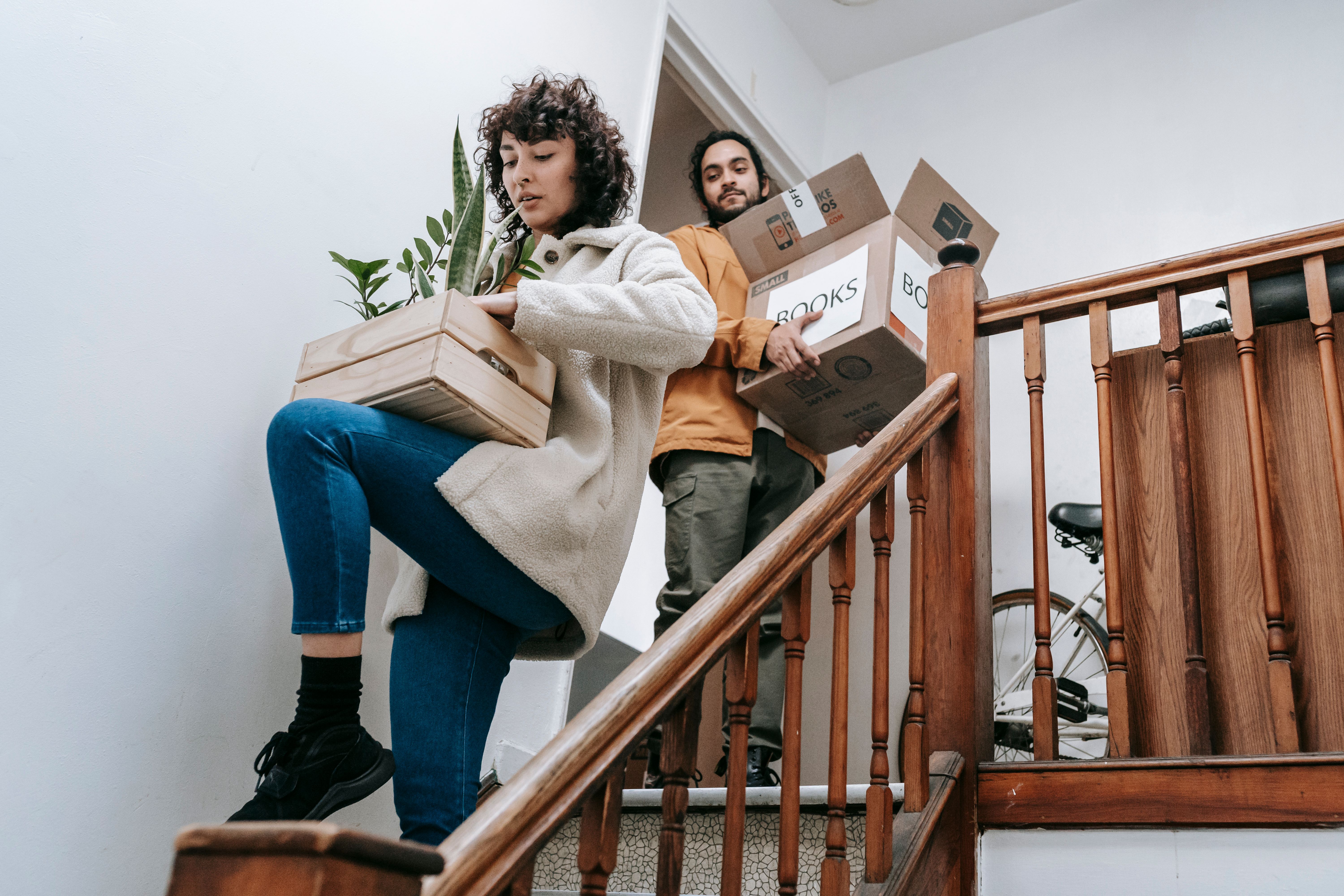 Two%20tenants%20moving%20out,%20going%20down%20a%20flight%20of%20stairs%20with%20boxes%20and%20a%20planter Two tenants moving out, going down a flight of stairs with boxes and a planter